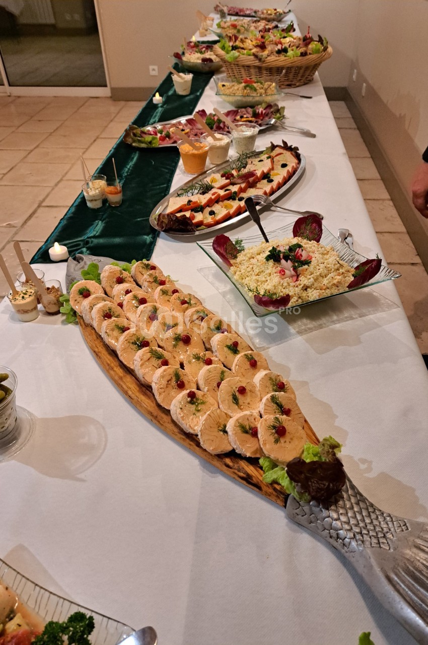 Buffet avec plats variés, incluant terrines, salades et desserts, disposés sur une table blanche dans une salle éclairée.