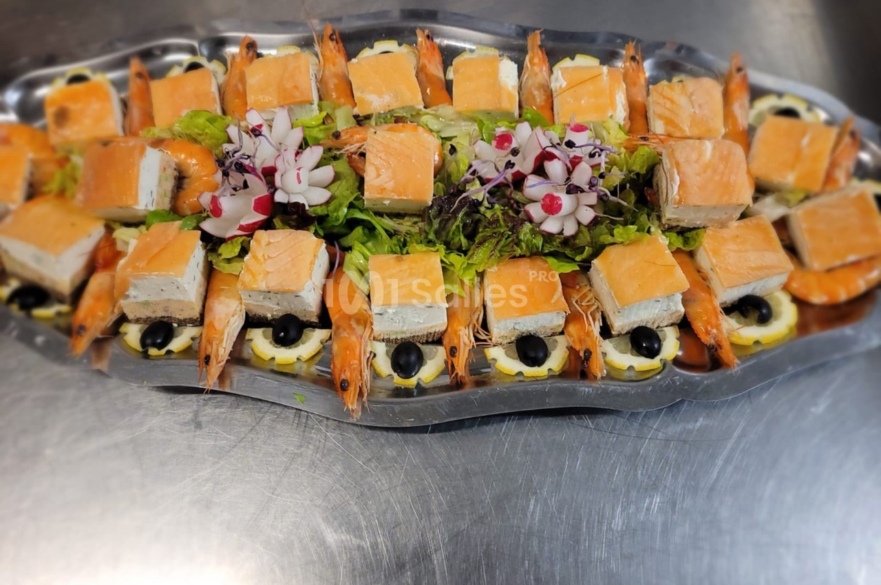 Plateau de saumon fumé, crevettes, olives noires et garniture de salade verte, décoré de fleurs comestibles.