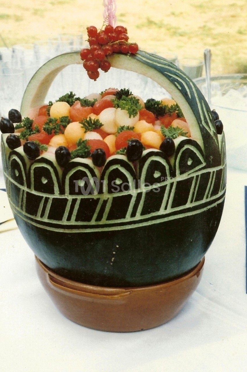 Panier sculpté dans une pastèque, rempli de billes de fruits colorés, décoré de groseilles et de persil.