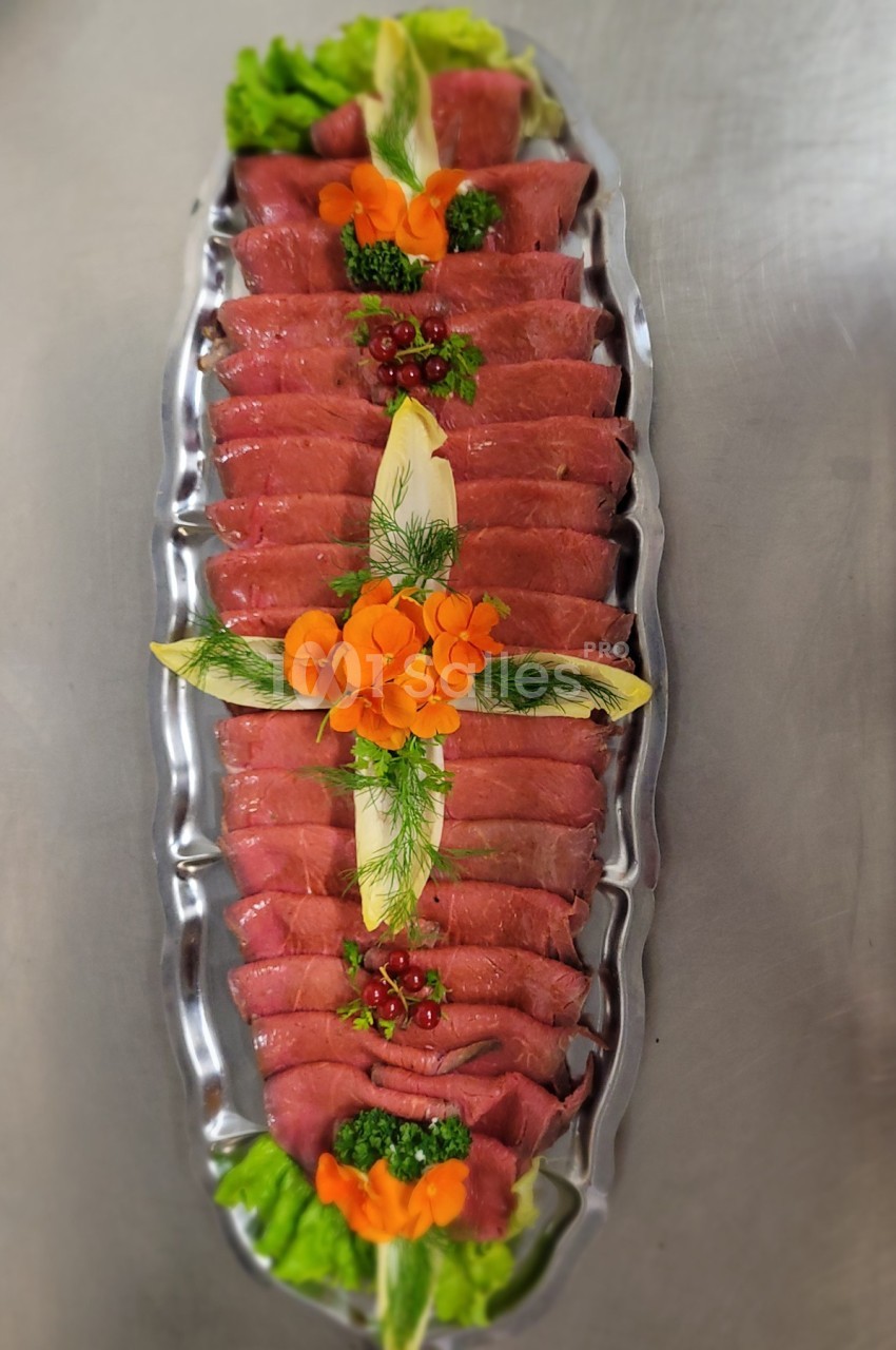 Plateau de carpaccio de bœuf présenté avec des garnitures de légumes, herbes fraîches et baies rouges.
