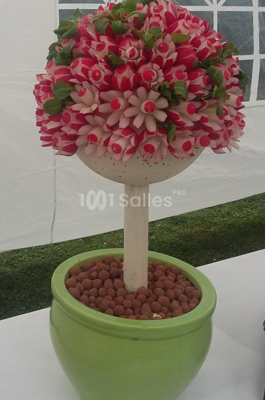 Arrangement de radis sculptés en forme de fleurs, monté sur un support dans un pot vert rempli de billes d'argile.