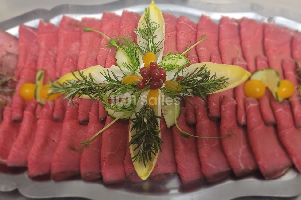 Plateau de tranches de rôti de bœuf garnies de feuilles d'endive, herbes fraîches et baies rouges.