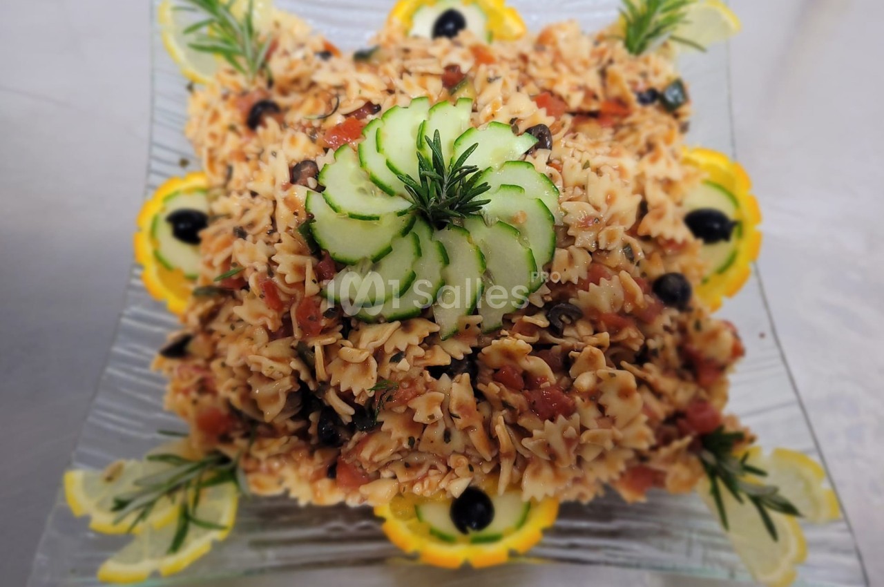 Assiette de pâtes farfalle garnie de légumes, olives noires, rondelles de concombre et décorations de citron.