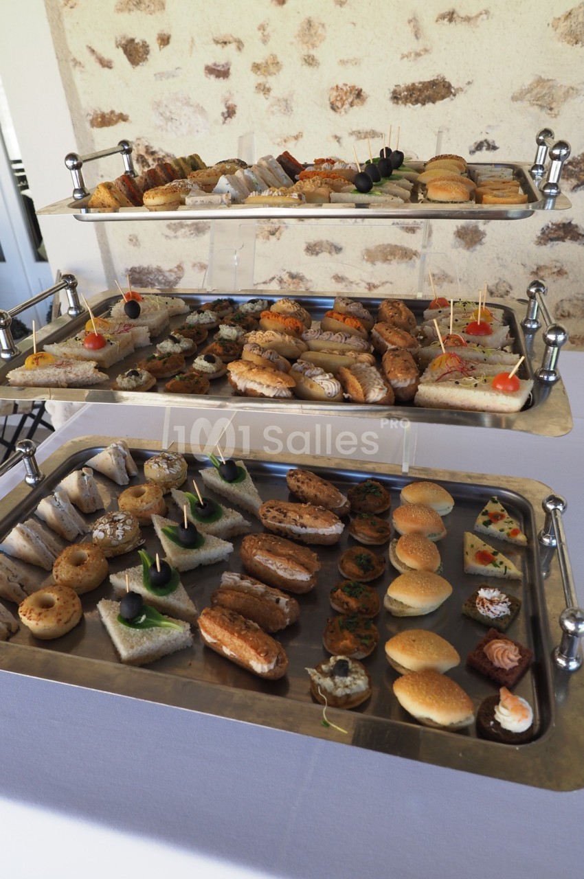 Plateaux garnis de canapés variés, mini-sandwichs et amuse-bouches disposés sur une table blanche.
