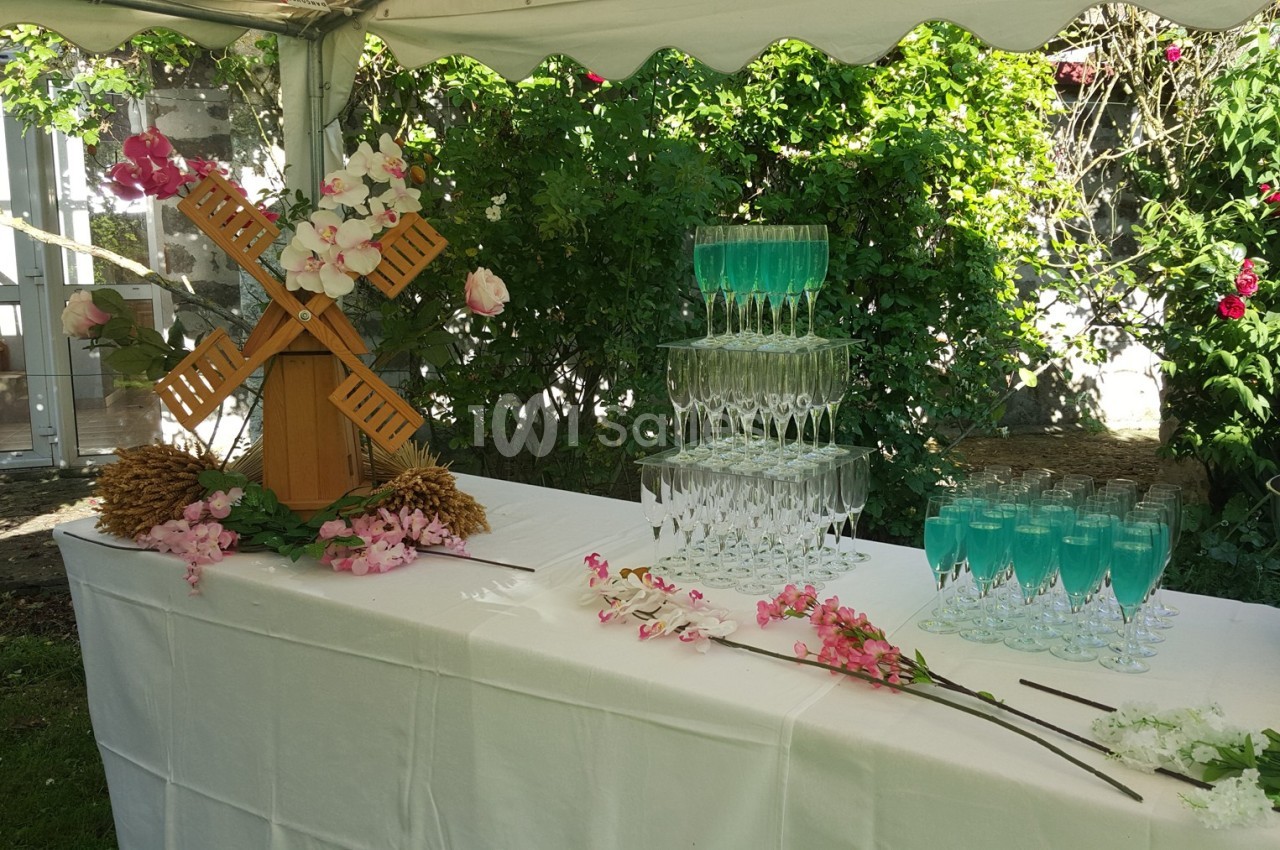 Table décorée avec un moulin miniature, des fleurs et une pyramide de verres remplis de boissons bleues, en extérieur.