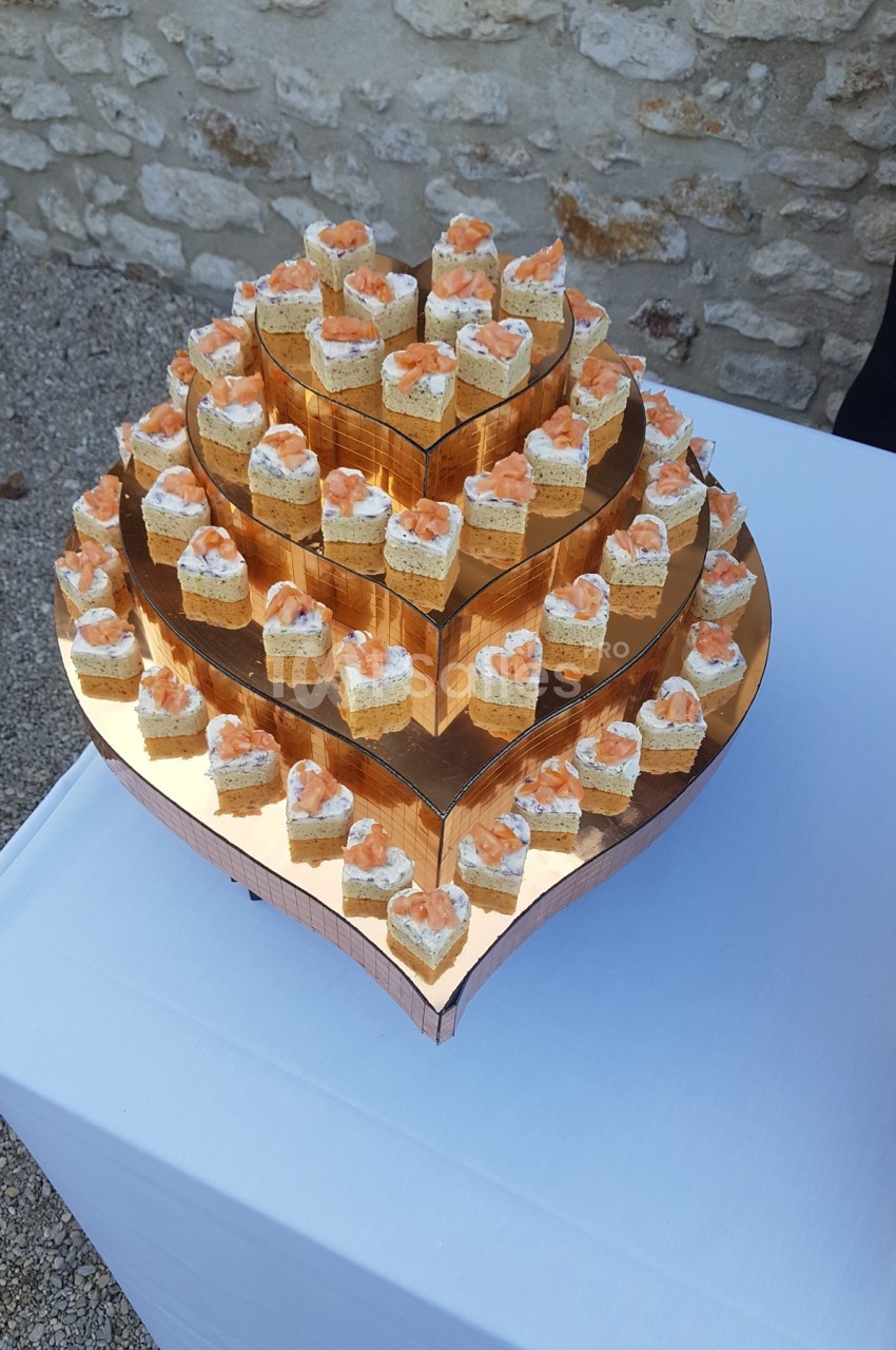 Plateau en forme de cœur avec des bouchées apéritives au saumon et crème disposées sur plusieurs niveaux.