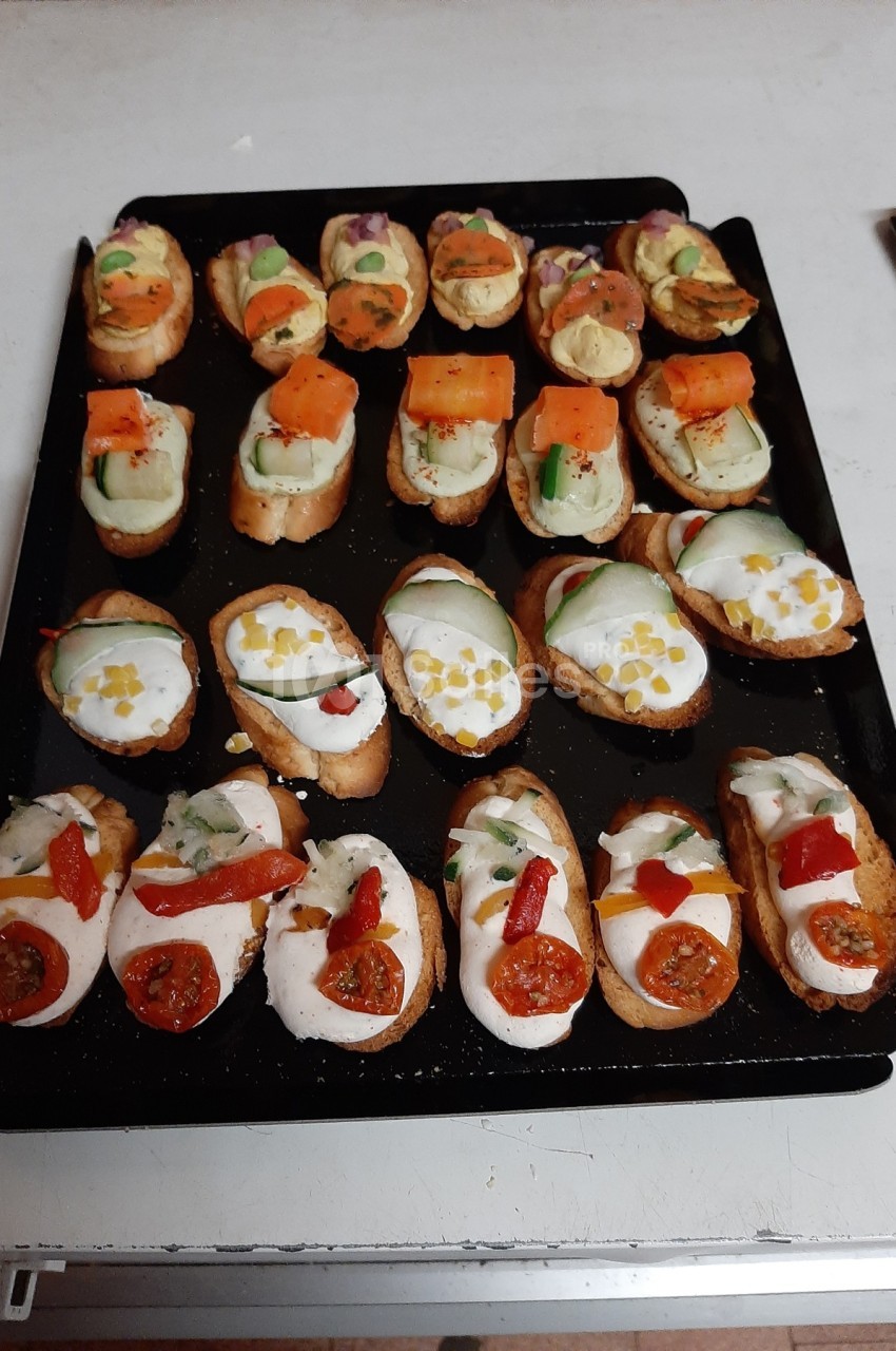 Plateau de bruschettas variées garnies de légumes, fromage et herbes, disposées sur une plaque noire.