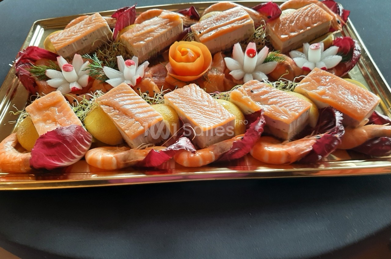 Plateau de saumon fumé avec crevettes, citron, fleurs sculptées et décoration de feuilles rouges sur un fond noir.