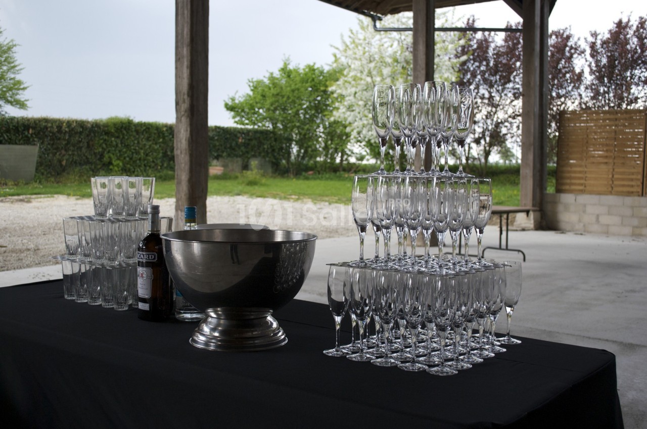 Table avec une nappe noire, contenant une pyramide de verres à champagne, une coupe en métal et des bouteilles.