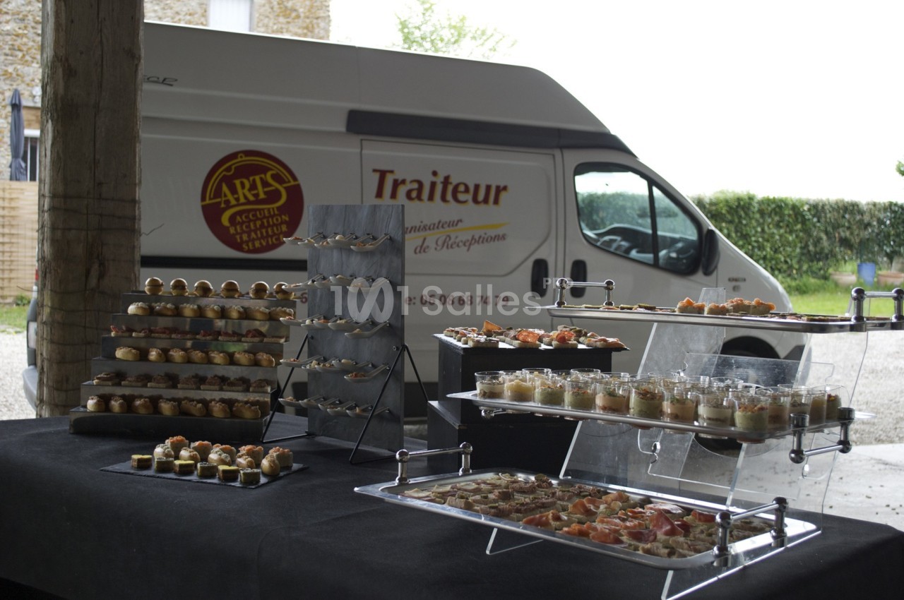 Buffet de canapés et verrines disposé sur des présentoirs devant un véhicule de traiteur stationné.