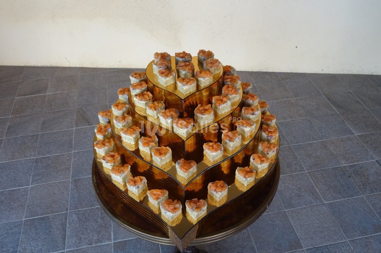 Présentoir en forme de cœur avec plusieurs étages de petits gâteaux individuels décorés, posé sur un sol carrelé.