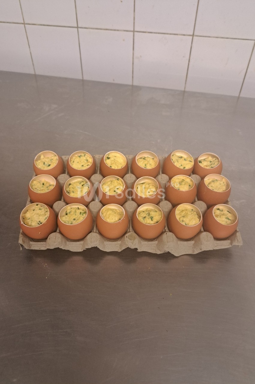 Plateau de coquilles d'œufs garnies d'une préparation culinaire, posé sur une surface métallique dans une cuisine.