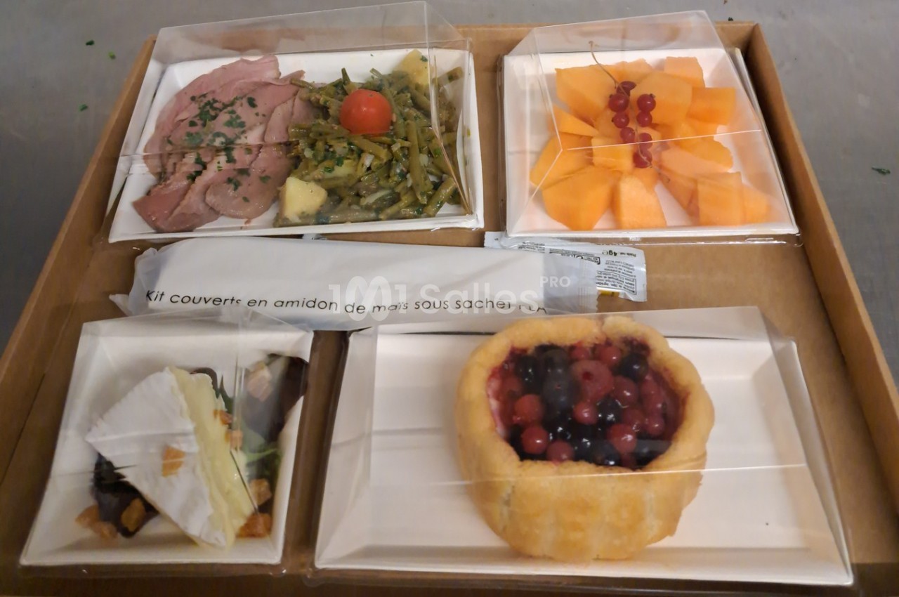 Plateau-repas composé de viande, légumes, fromage, dessert aux fruits rouges et salade de melon, avec couverts inclus.