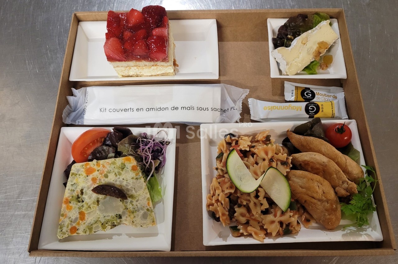Plateau-repas composé de légumes, pâtes, fromage, dessert aux fraises et couverts emballés sur une table.