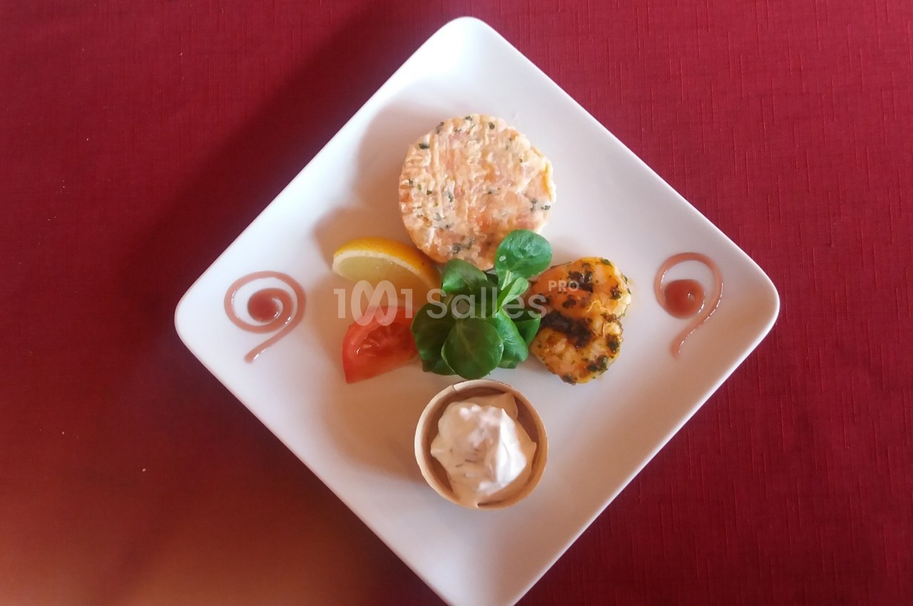 Assiette carrée avec un tartare de poisson, une garniture de légumes, une sauce, une tranche de citron et des décorations.