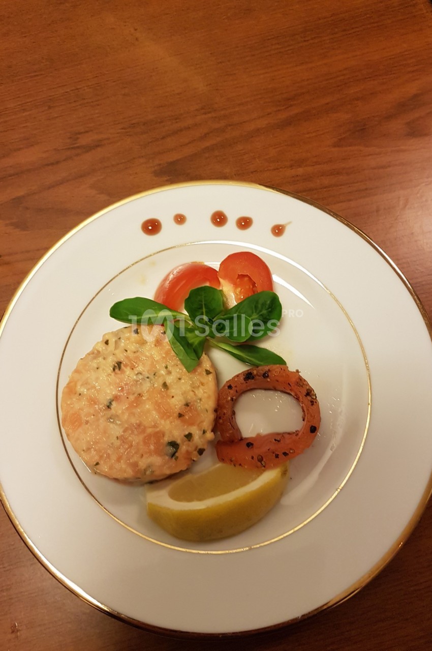 Assiette avec un tartare de saumon, rondelle de poivron grillé, citron, mâche, tomate et décor de sauce.