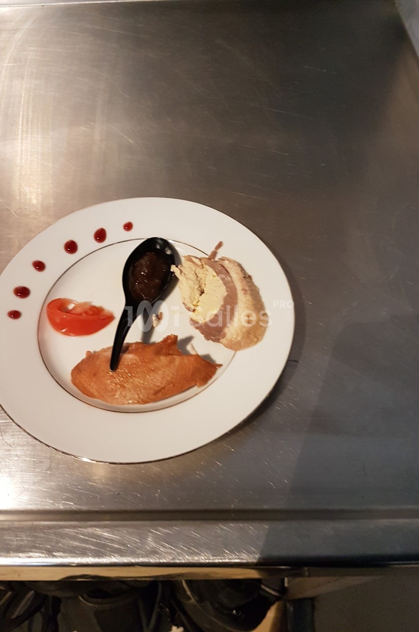 Assiette contenant une tranche de viande, une purée, une sauce dans une cuillère noire, tomate et points de sauce rouge.