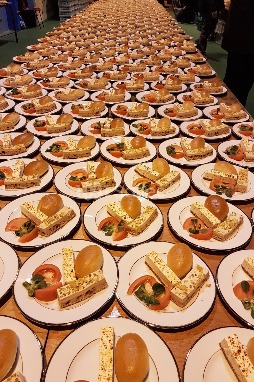 Des assiettes identiques alignées avec des desserts composés de brioche, nougat glacé et garniture de fruits.
