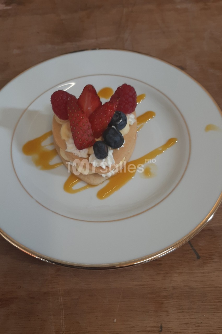 Assiette avec un dessert composé de pancakes garnis de crème, fraises, framboises, myrtilles et coulis de mangue.