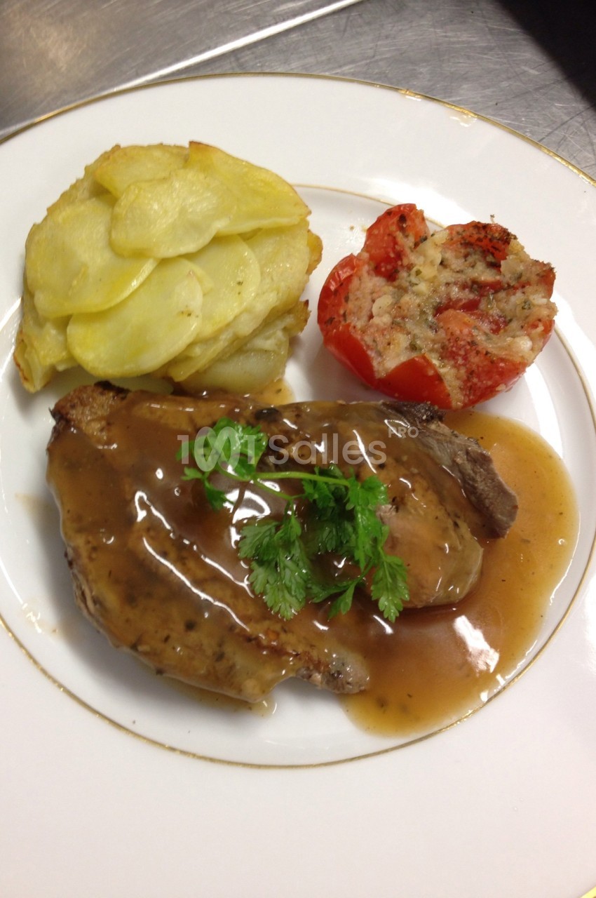 Assiette avec viande en sauce, gratin de pommes de terre et tomate farcie, servie sur une table.