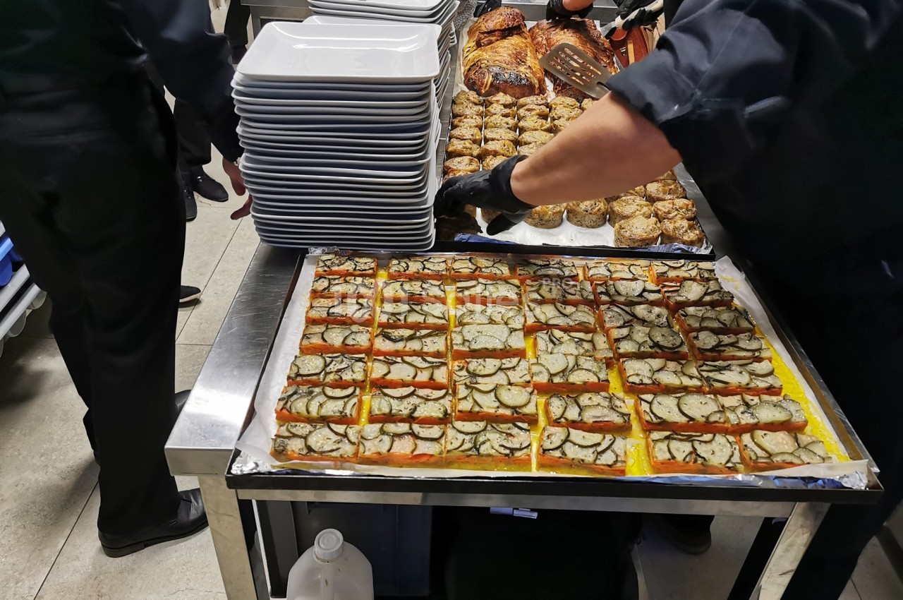 Des cuisiniers préparent des plats en cuisine, avec des tartes salées garnies de légumes sur une table en inox.