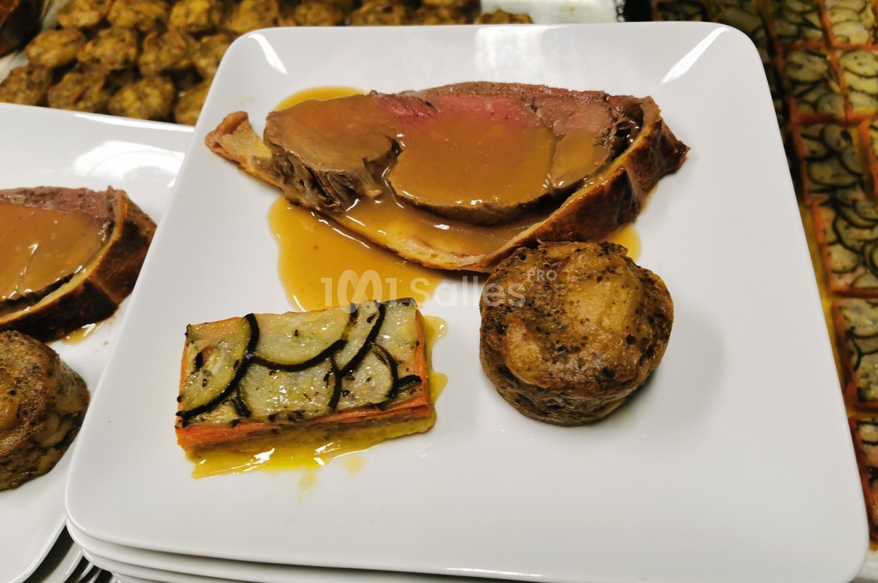 Assiette avec une tranche de viande en croûte et sauce, un gratin de légumes et une pomme de terre rôtie.