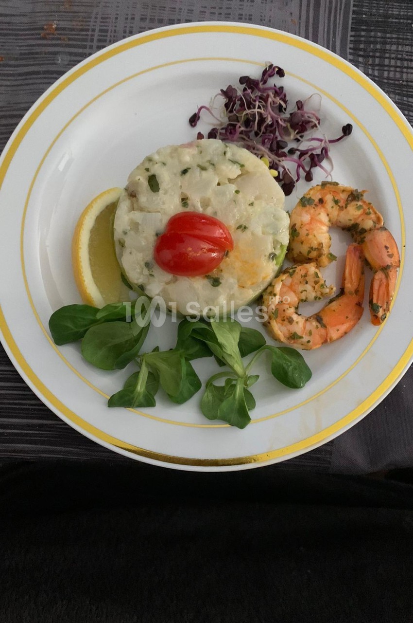 Assiette composée d'un tartare de poisson, crevettes marinées, mâche, germes de radis et tranche de citron.