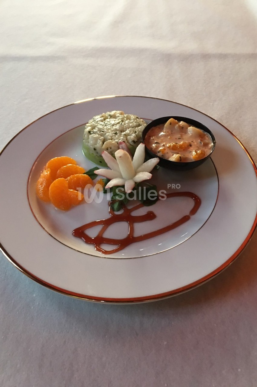 Assiette contenant un tartare, des quartiers de mandarine, une décoration florale et une sauce en ramequin.