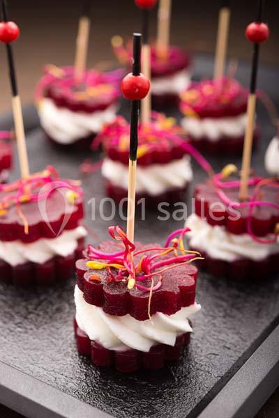 Tranches de betterave en forme de fleur garnies de fromage frais, décorées de pousses et piquées sur un plateau noir.