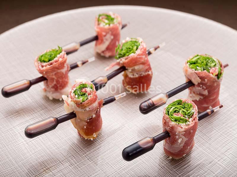 Roulés de jambon cru garnis de verdure, présentés sur des pipettes contenant une sauce.
