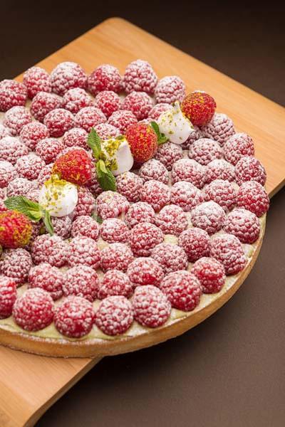 Tarte garnie de framboises fraîches, fraises, crème et feuilles de menthe, saupoudrée de sucre glace.