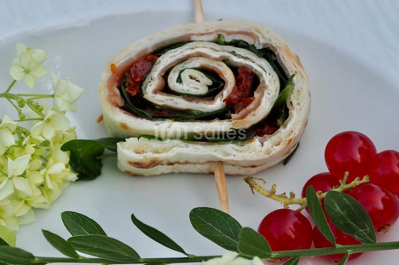 Roulé de tortilla garni de légumes et épinards, présenté sur une assiette avec tomates cerises et fleurs décoratives.