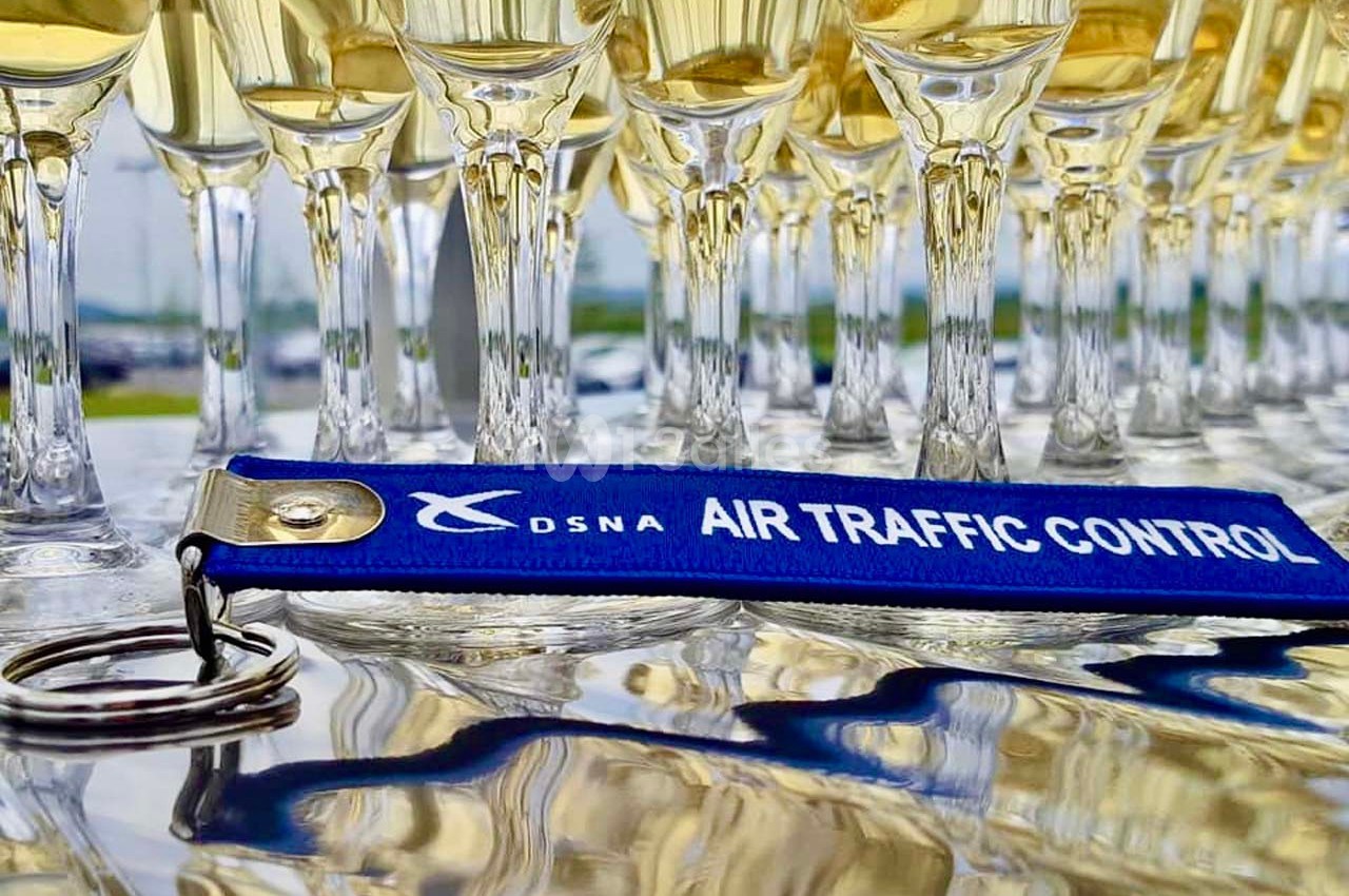 Rangée de verres de champagne alignés sur une table avec un porte-clés bleu marqué ’DSNA Air Traffic Control’.