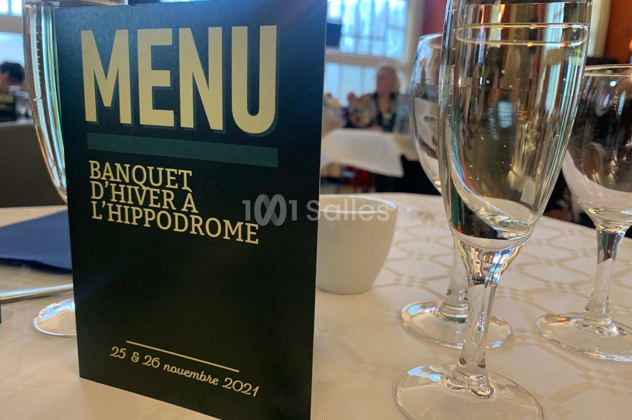 Carte de menu posée sur une table dressée avec des verres et un fond flou de salle de banquet.