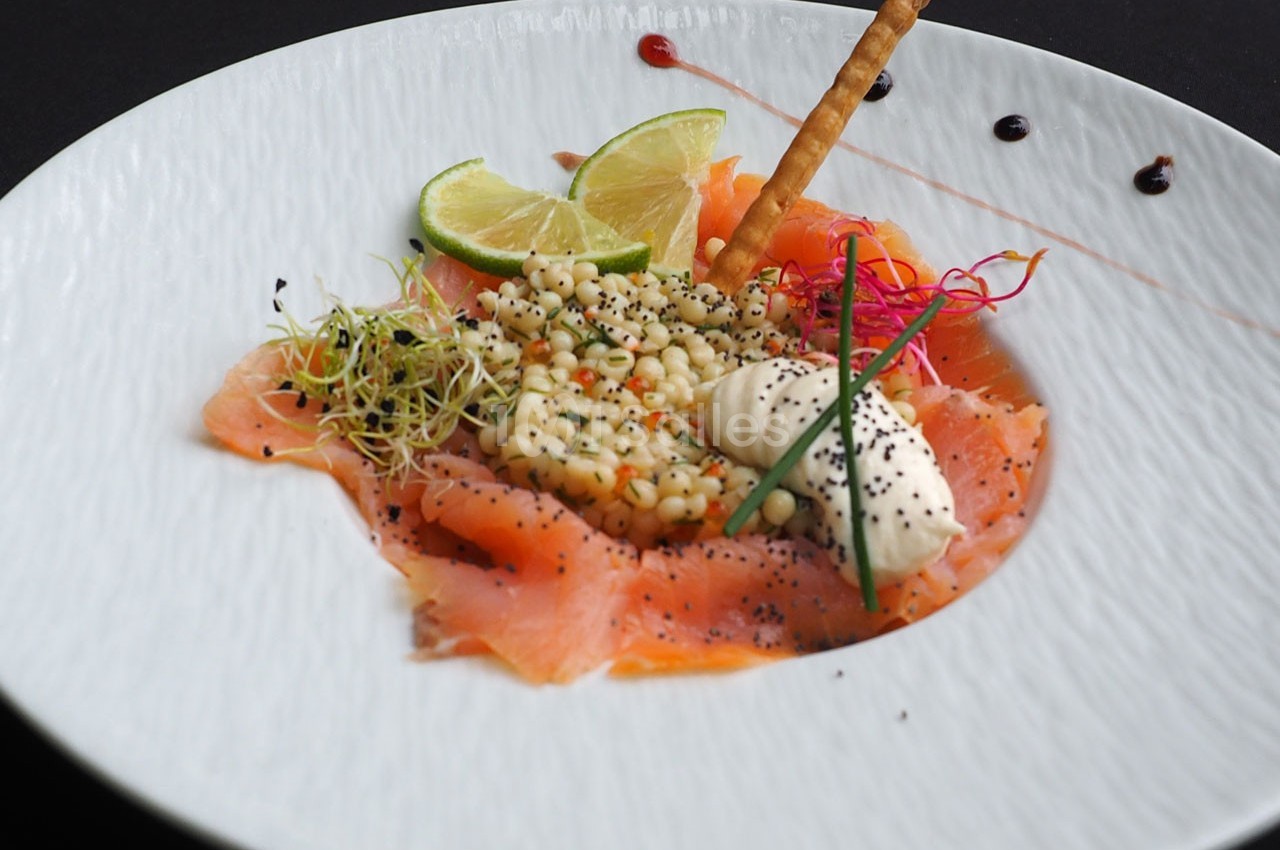 Assiette de saumon fumé avec crème, salade de perles, citron vert, graines et décorations colorées.