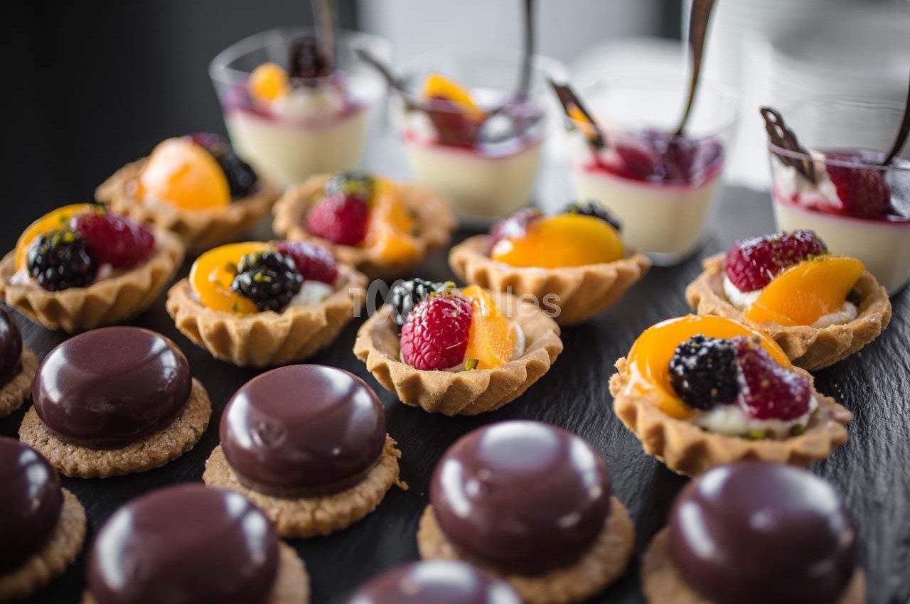 Assortiment de desserts comprenant tartelettes aux fruits, entremets au chocolat et verrines aux fruits rouges.