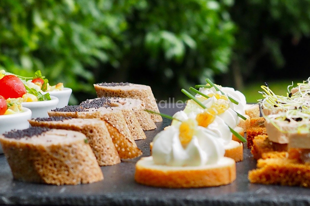 Assortiment de canapés variés disposés sur une ardoise, avec un fond flou de verdure.