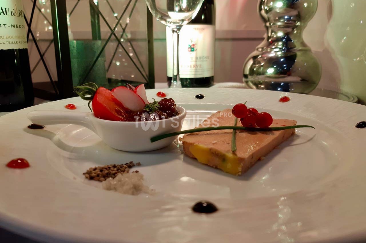 Assiette gastronomique avec foie gras, chutney, radis, groseilles et décorations, servie sur une table élégante.