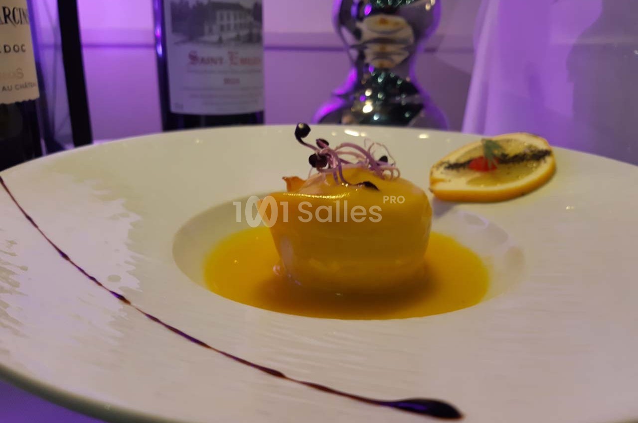 Dessert élégant présenté dans une assiette blanche, nappé de sauce jaune, décoré de micro-pousses et d'une tranche d'orange.