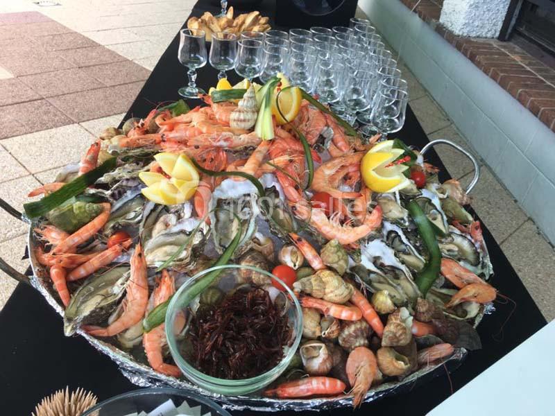 Plateau de fruits de mer variés avec crevettes, huîtres, bulots, citrons et légumes, disposé sur une table.