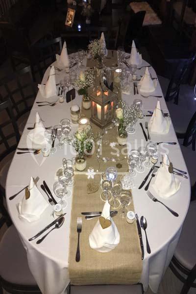 Table décorée pour un dîner, avec nappes blanches, serviettes pliées, lanternes, fleurs et couverts disposés.