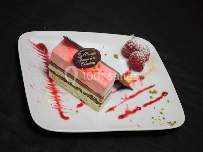 Part de gâteau colorée avec couches de mousse, chocolat et pistache, décorée de framboises et coulis rouge sur une assiette…