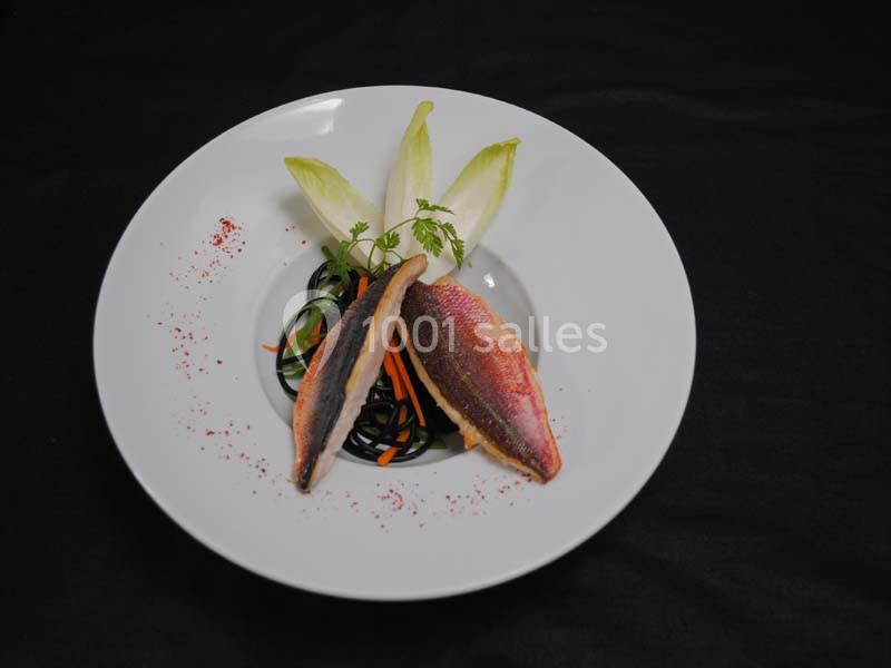 Assiette avec filets de poisson, pâtes noires, julienne de carottes, endives et herbes, sur fond noir.