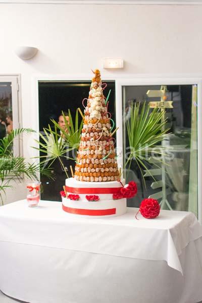 Pièce montée en choux décorée de fleurs rouges, posée sur une table blanche dans une salle lumineuse.