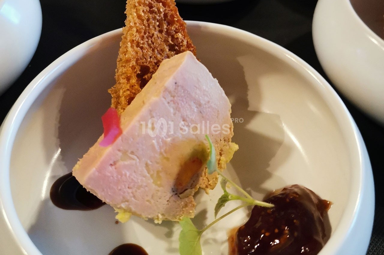 Part de foie gras servie avec une tranche de pain grillé, une sauce brune et une touche de verdure dans une assiette blanche.
