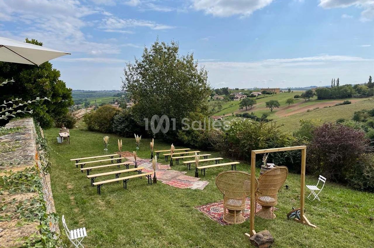 Chaises et bancs disposés en extérieur sur une pelouse, avec vue sur la campagne, pour une cérémonie ou un événement.