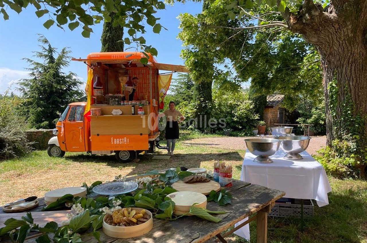 Un food truck orange dans un cadre champêtre avec des tables dressées pour un service en extérieur.