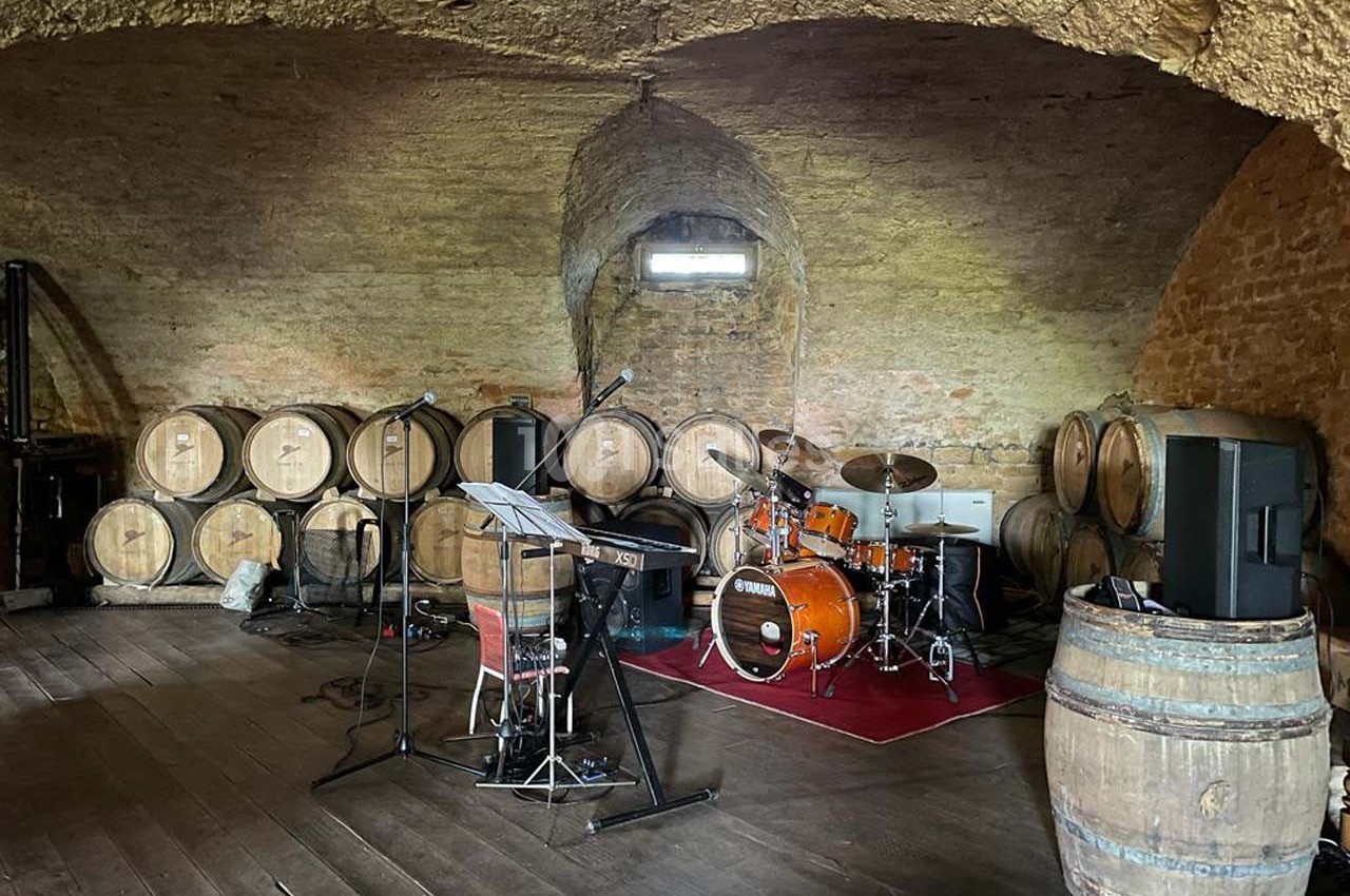 Salle voûtée avec barriques en bois, équipée d'instruments de musique dont une batterie et des micros.