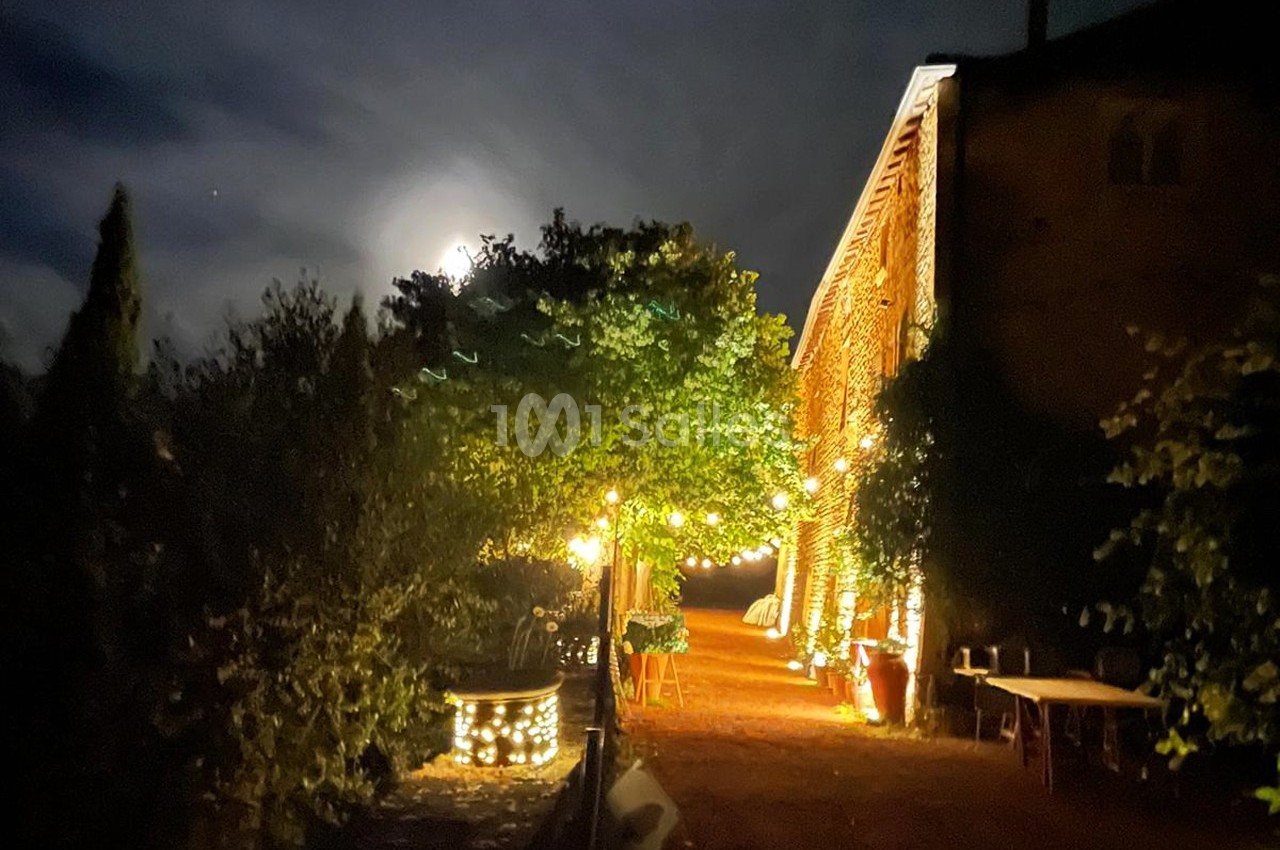 Cour éclairée par des guirlandes lumineuses près d'un bâtiment en pierre, avec la lune visible dans un ciel nocturne.
