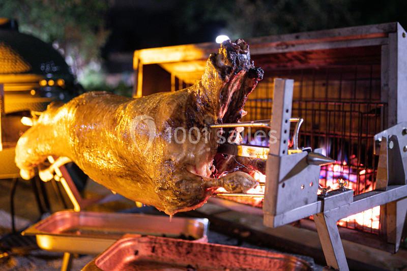 Un agneau entier rôti à la broche devant un feu de bois, dans un cadre extérieur nocturne.